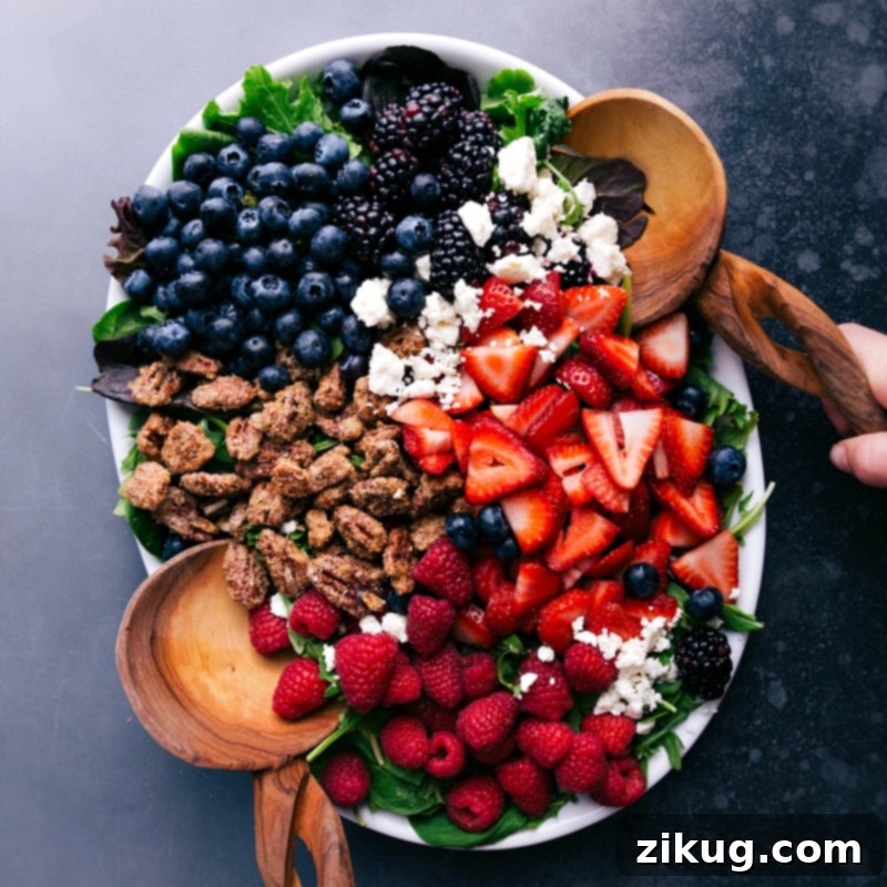 A vibrant and healthy raspberry salad, richly topped with homemade vinaigrette, candied pecans, and feta, presented on a white plate.