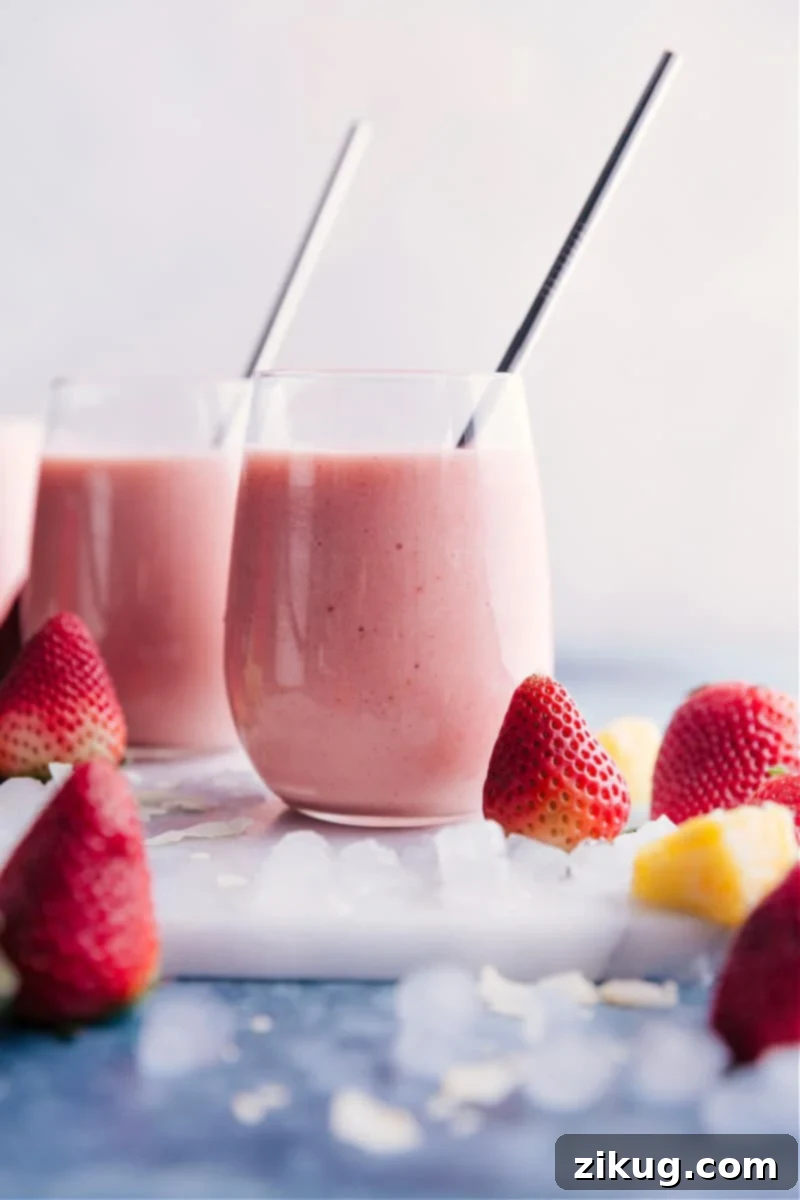 Two glasses of creamy, sweet Strawberry Piña Colada smoothies garnished with fresh strawberries and pineapple wedges, set against a bright, tropical background.