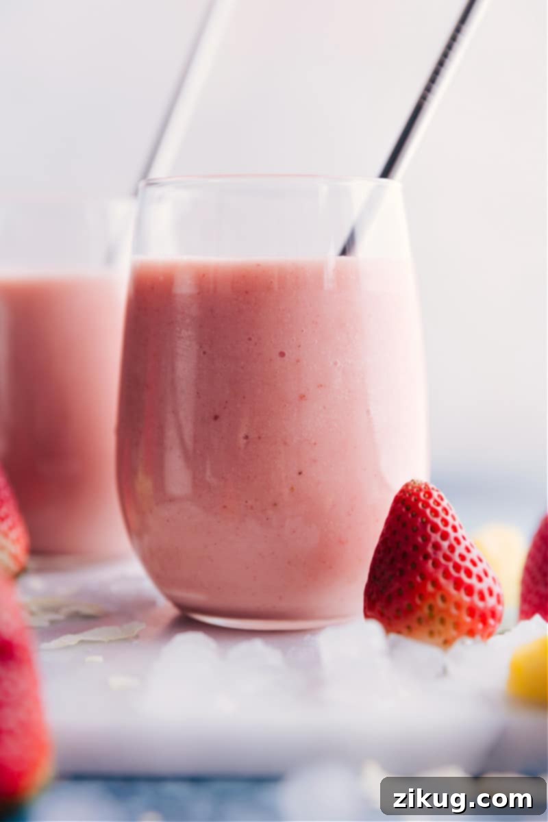 Two vibrant Strawberry Piña Colada smoothies in tall glasses, garnished with fresh strawberries and pineapple leaves, ready to be enjoyed.