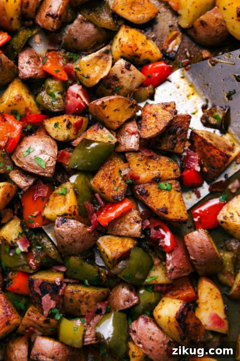 Easy One Pan Bacon and Potatoes 2 Close-up of golden brown oven-roasted breakfast potatoes and crispy bacon with colorful bell peppers and onions on a sheet pan, ready to eat.