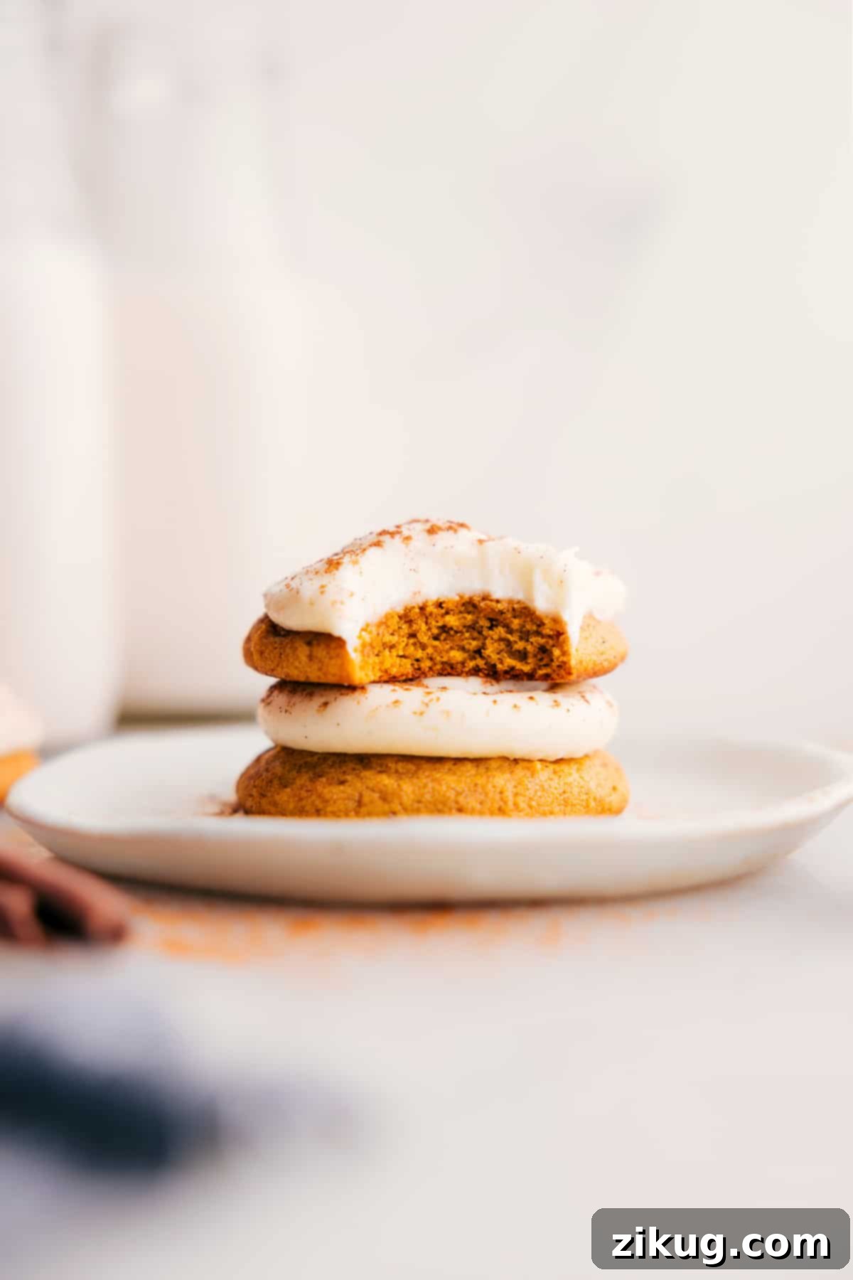 The Best Pumpkin Cookies with Cream Cheese Frosting Pumpkin Cookies with Cream Cheese Frosting stack on a plate, the top one with a bite missing.