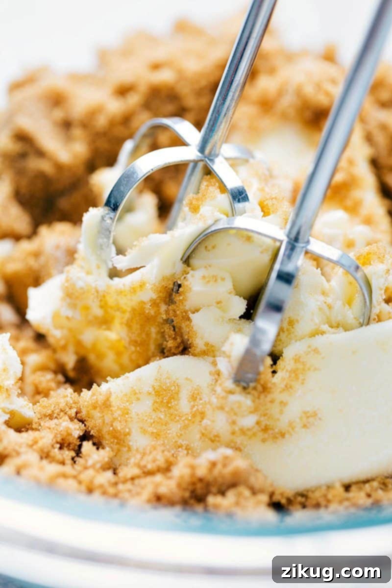 Softened butter and granulated sugar being thoroughly beaten in a large mixing bowl with an electric mixer, forming a light and fluffy mixture.