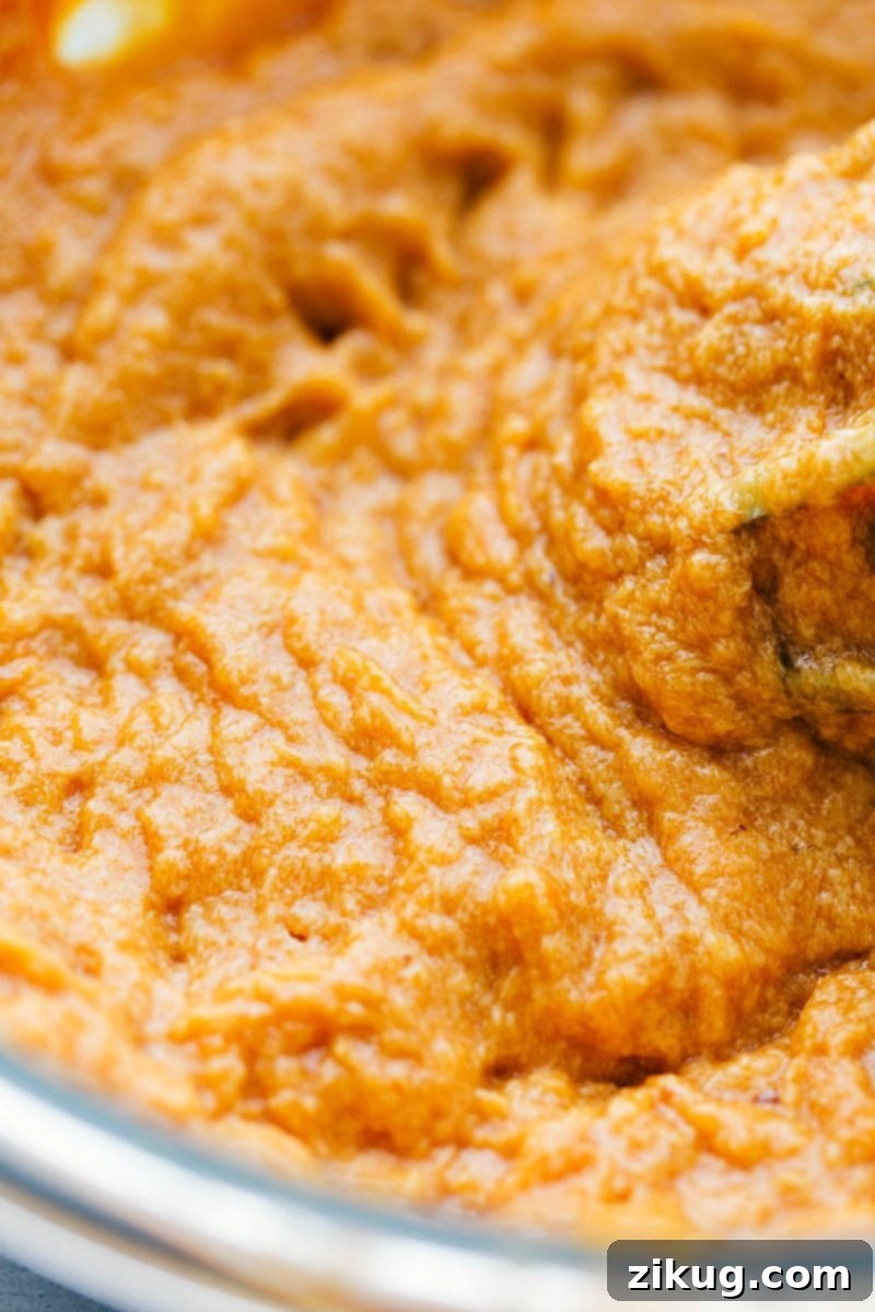 The process of adding canned pumpkin puree to a bowl of wet batter mixture, with a spatula visible.