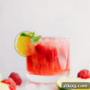 A close-up of a glass of Sparkling Raspberry Limeade, garnished with fresh raspberries and lime, highlighting its vibrant color and refreshing appeal.