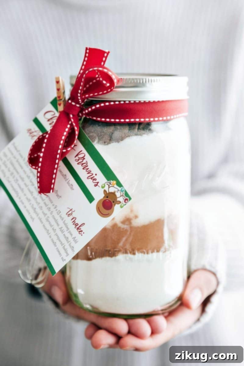 Beautifully layered Christmas brownie mix in a clear Mason jar, adorned with festive ribbon, ready for gifting, accompanied by a free printable recipe tag.