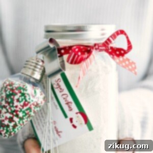 Homemade Mason Jar Sugar Cookies 5 A baked sugar cookie with sprinkles, positioned next to a mason jar filled with cookie mix ingredients.