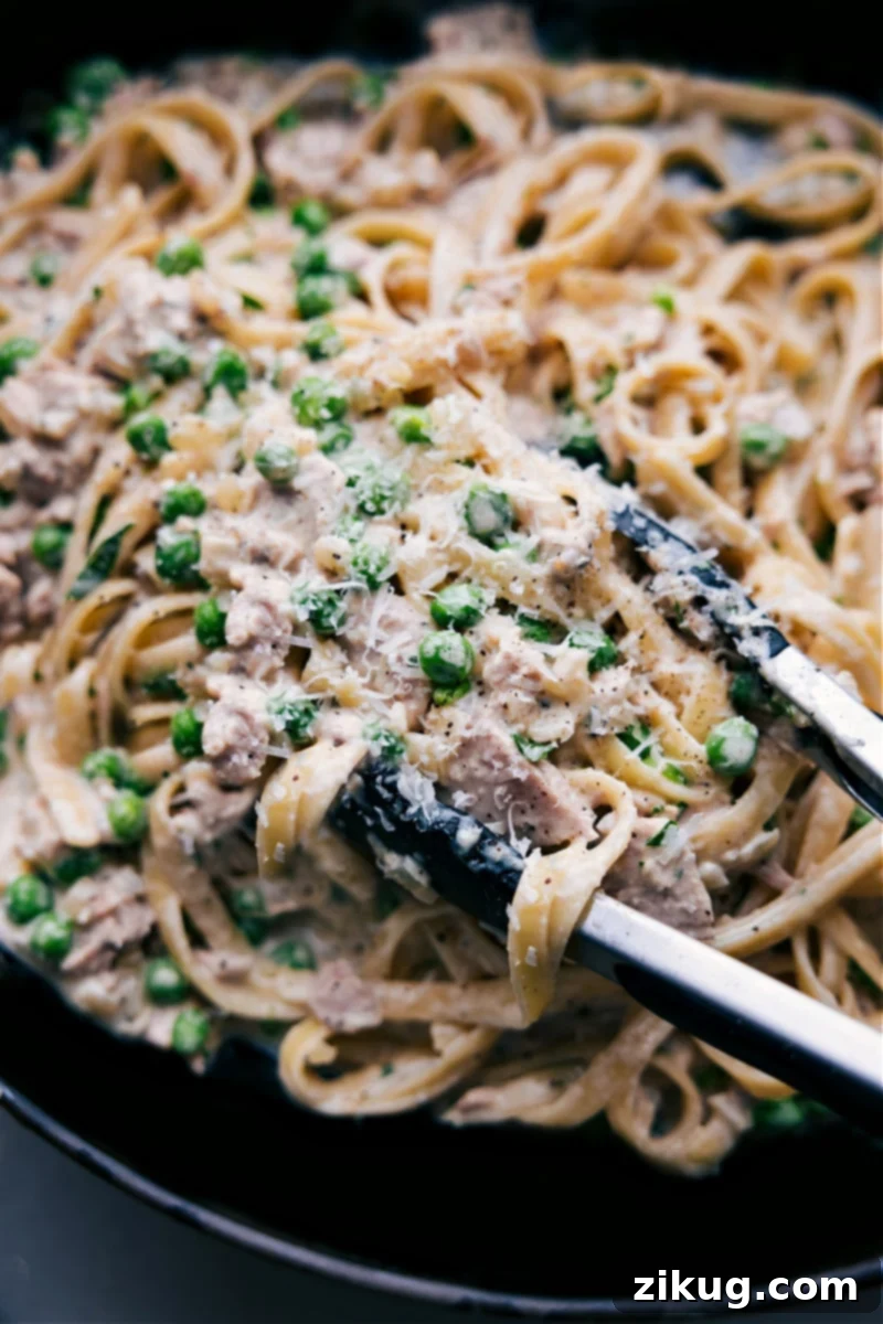 Delicious Creamy Tuna Pasta: Fettuccine, sweet peas, garlic-Parmesan sauce, and olive oil tuna for a quick, comforting meal. Overhead image of the creamy tuna pasta with fresh parsley and lemon wedges, ready to serve
