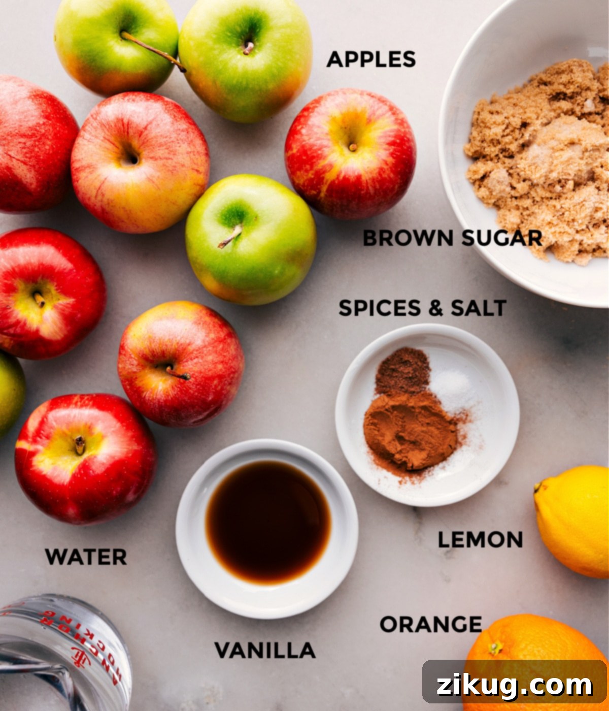 Fresh ingredients for a delightful apple-infused drink: a variety of apples, rich brown sugar, pure vanilla extract, and an assortment of aromatic spices arranged beautifully.