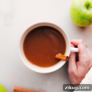 Hand holding a warm cup of apple cider with steam rising.