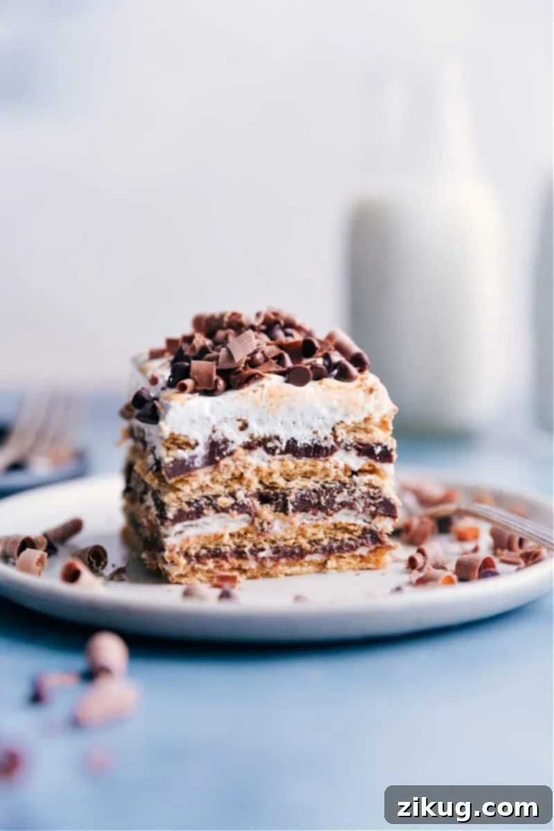 S'mores Icebox Cake: A no-bake delight with layers of chocolate ganache, marshmallow cream, and honey graham crackers. Perfect for summer! #smores #iceboxcake #nobake #dessert #chocolate #marshmallow #grahamcrackers A beautifully presented slice of S'mores Icebox Cake on a white plate, showcasing its distinct layers of graham crackers, chocolate, and marshmallow, topped with toasted meringue.