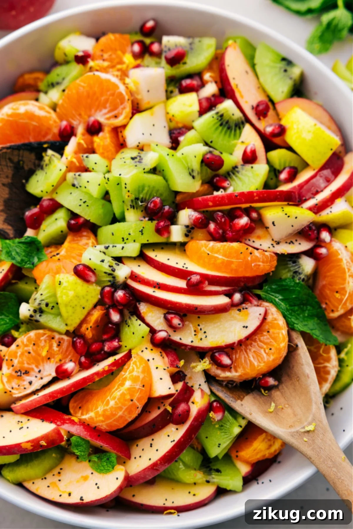 Delicious Winter Fruit Salad With In-Season Fruit Winter fruit salad in a large glass bowl, dressed and ready to enjoy, garnished with fresh mint.