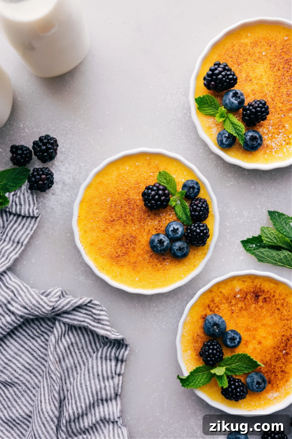 Golden creme brûlées with a crisp sugary top, garnished with fresh fruit, invitingly presented.