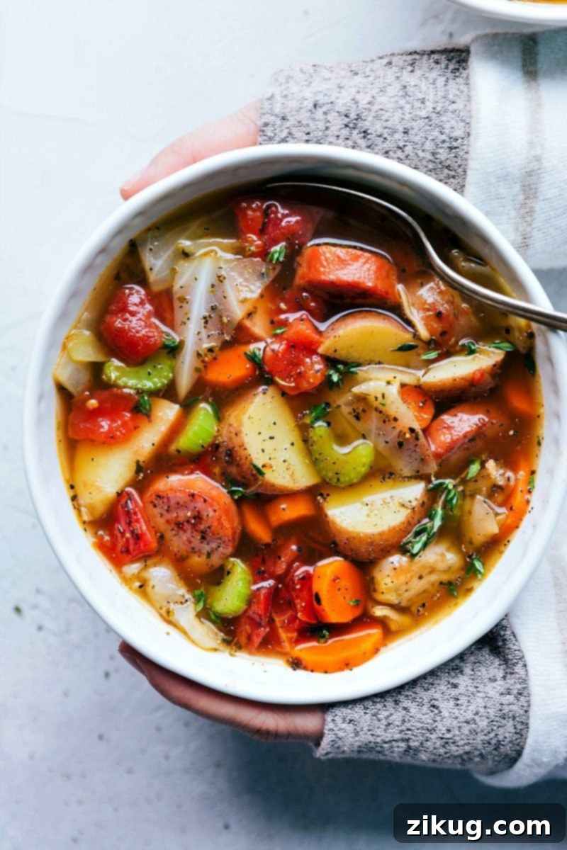 A close-up of a large pot of simmering sausage, potato, and cabbage soup, showing the rich broth and tender ingredients. This healthy, easy, and quick recipe features turkey sausage, making it kid-friendly and perfect for a cozy meal. chelseasmessyapron.com
