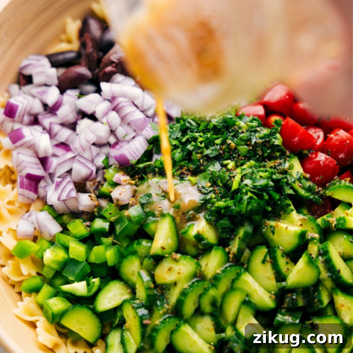 Vibrant Mediterranean Pasta Salad 4 The dressing being poured over the Greek Pasta Salad in a large bowl.