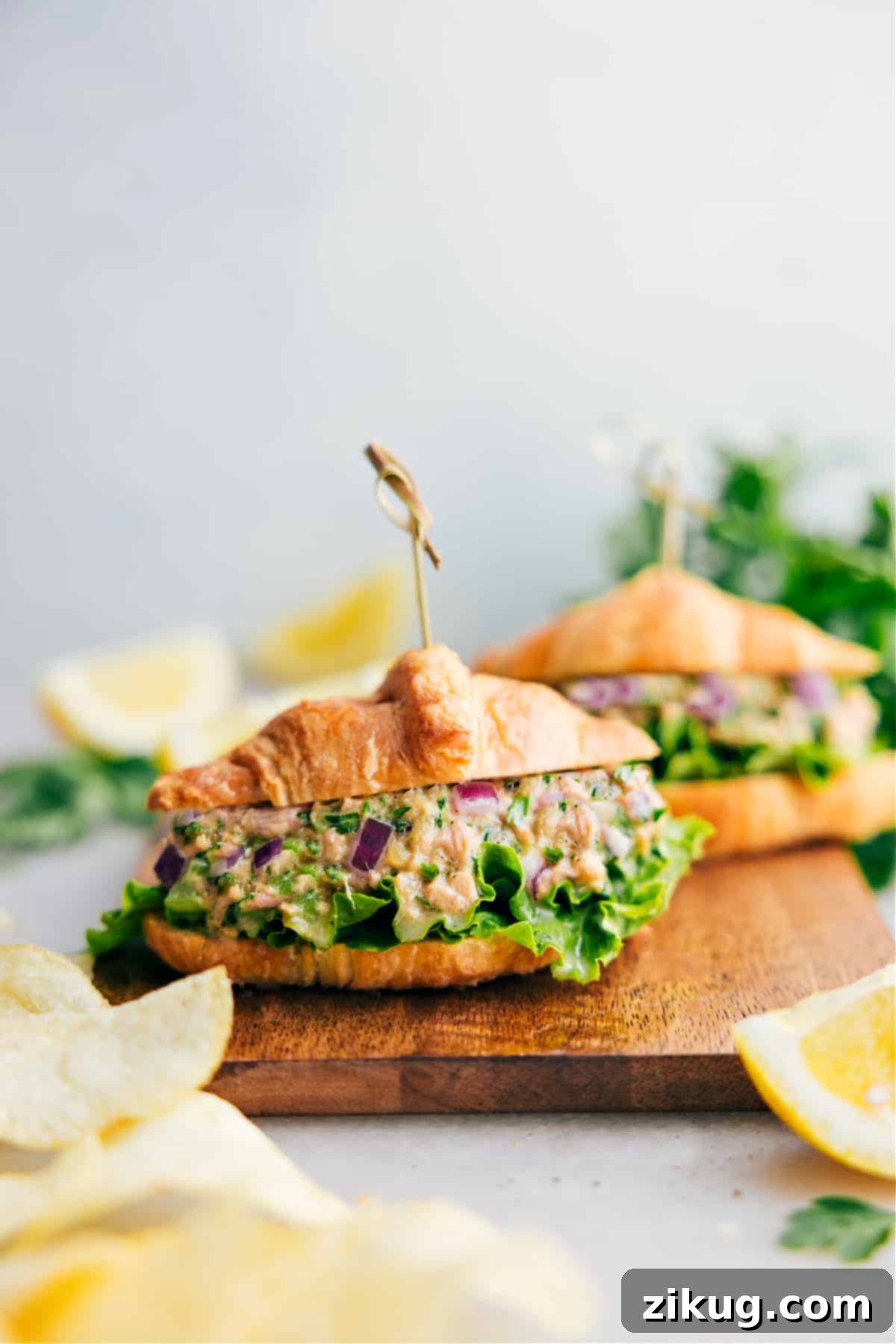 The Absolute Best Tuna Salad Croissant A serving of the absolute best creamy tuna salad, artfully presented on a flaky croissant, garnished with fresh parsley, ready to be enjoyed.