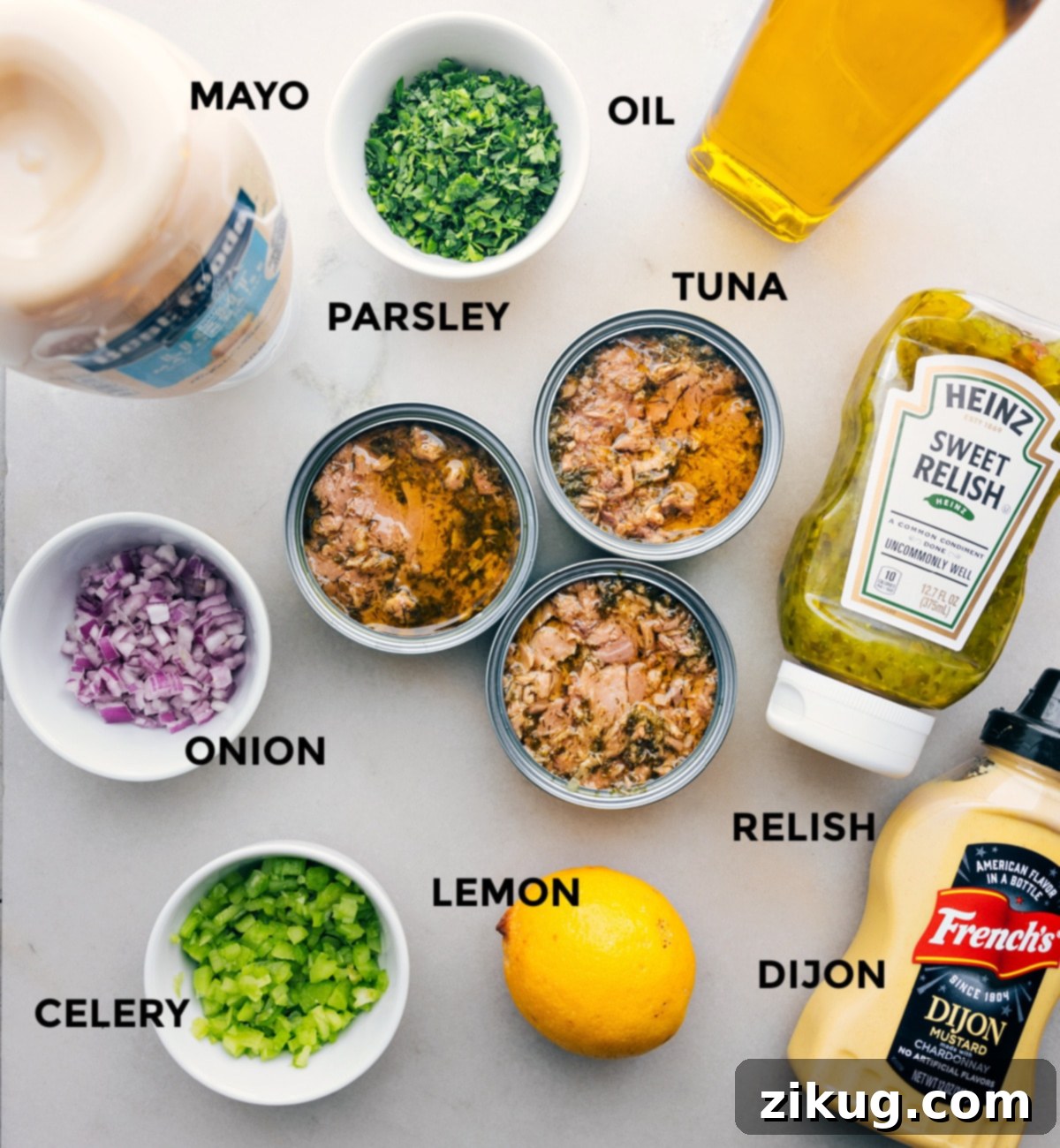 Assembled Tuna Salad Ingredients All the essential ingredients for making the best tuna salad are neatly laid out on a clean counter, including creamy mayonnaise, vibrant fresh parsley, golden olive oil, canned tuna, crisp red onion, tangy pickle relish, a fresh lemon, savory Dijon mustard, and crunchy celery stalks.