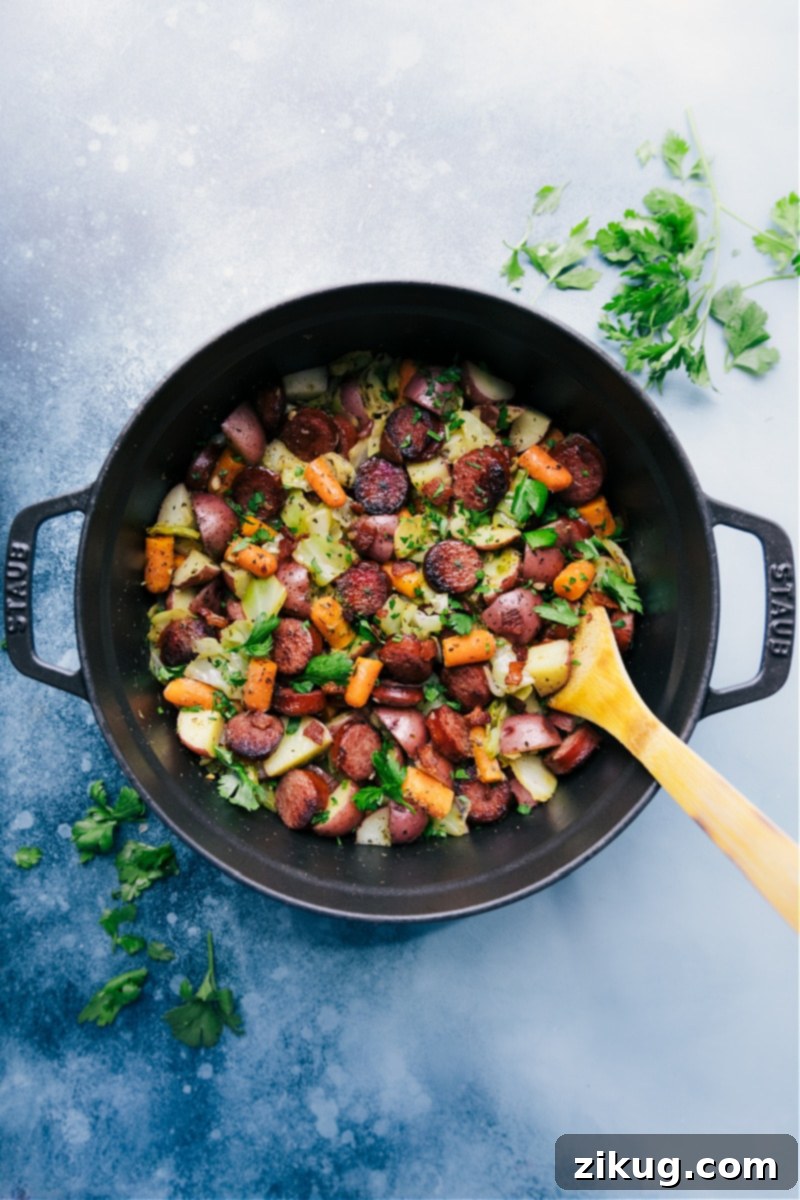 Rustic Cabbage Sausage and Potato Skillet 2 A large skillet filled with cooked cabbage, golden brown sausage slices, and tender baby red potatoes and carrots, garnished with fresh parsley.