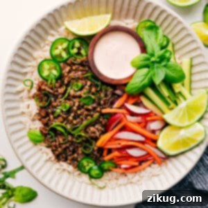 A vibrant Banh Mi Bowl featuring seasoned ground pork, quick-pickled carrots and radishes, fresh cucumber, and a creamy Sriracha-lime sauce over a bed of rice.