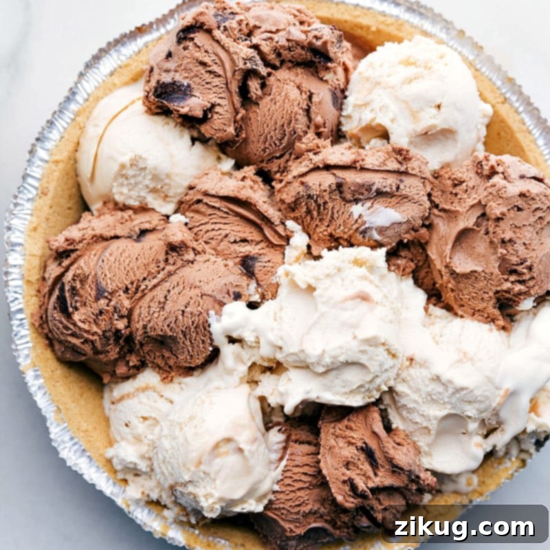 Scoops of Ice Cream in Pie Crust Ready to be Frozen Two distinct flavors of ice cream, chocolate and caramel, are carefully arranged in alternating scoops within a golden graham cracker pie crust, creating an appealing layered effect before the pie is frozen.