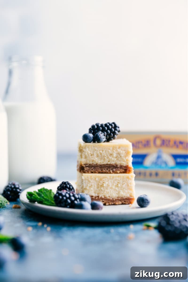 Stacked vanilla cheesecake bars topped with fresh berries and a drizzle of sauce, showcasing their thick graham cracker crust.
