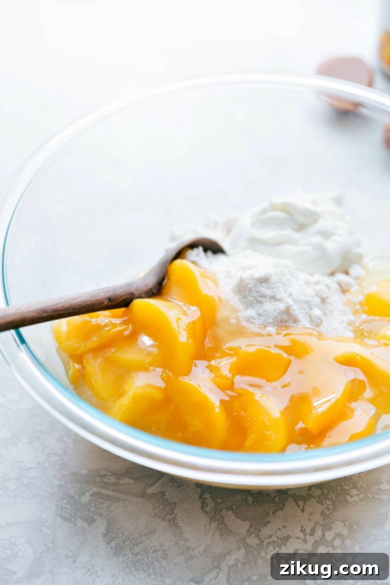 Mixing peaches with other ingredients for the cake batter A large mixing bowl containing vibrant yellow cake mix and glistening peach pie filling, being gently combined with a spatula for a homemade peaches and cream cake.