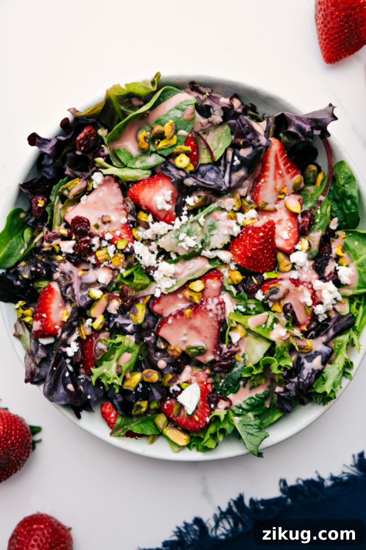 A beautifully composed, large salad, generously tossed and drizzled with the homemade Strawberry Vinaigrette, featuring a vibrant mix of fresh greens, an abundance of berries, sliced peaches, crunchy almonds, and crumbled goat cheese, ready for serving.