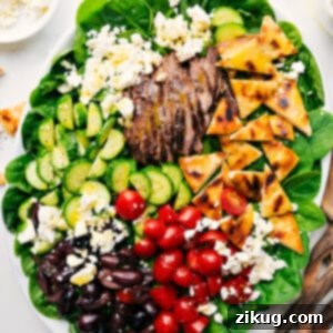 A close-up of the delicious Grilled Steak Salad, showcasing tender steak slices, crisp greens, feta, olives, and grilled pita, all drizzled with a bright lemon-honey vinaigrette.