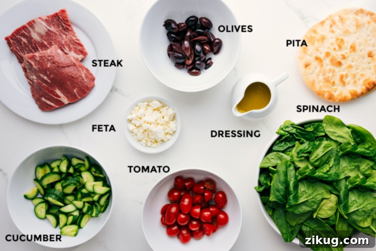 All the fresh ingredients prepped and arranged for easy assembly of the grilled steak salad, including thinly sliced grilled steak, Kalamata olives, grilled pita wedges, fresh baby spinach, a jar of honey-lemon dressing, crumbled feta cheese, bright cherry tomatoes, and sliced cucumber, laid out on a wooden board.
