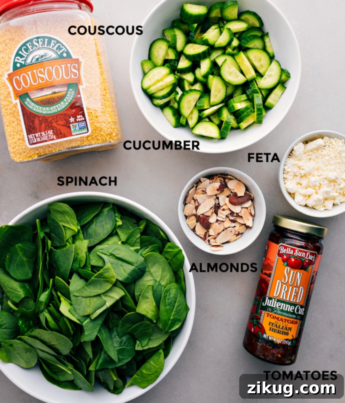 All the vibrant ingredients for the Couscous Mediterranean Salad—cucumber, feta cheese, toasted almonds, sun-dried tomatoes, fresh spinach, and fluffy couscous—prepped and ready for assembly.
