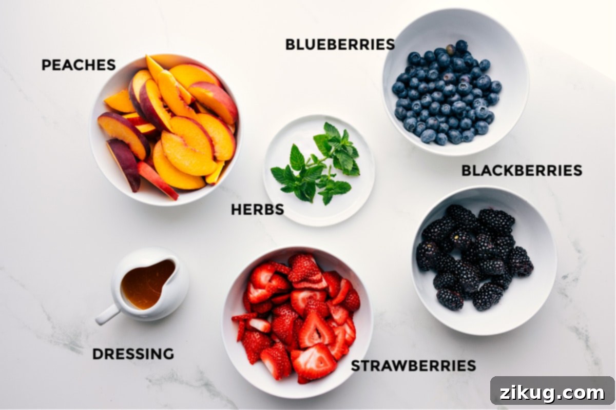 Fresh ingredients laid out for Peach Fruit Salad, including sliced peaches, strawberries, blueberries, blackberries, and fresh mint, alongside a jar of citrus dressing.