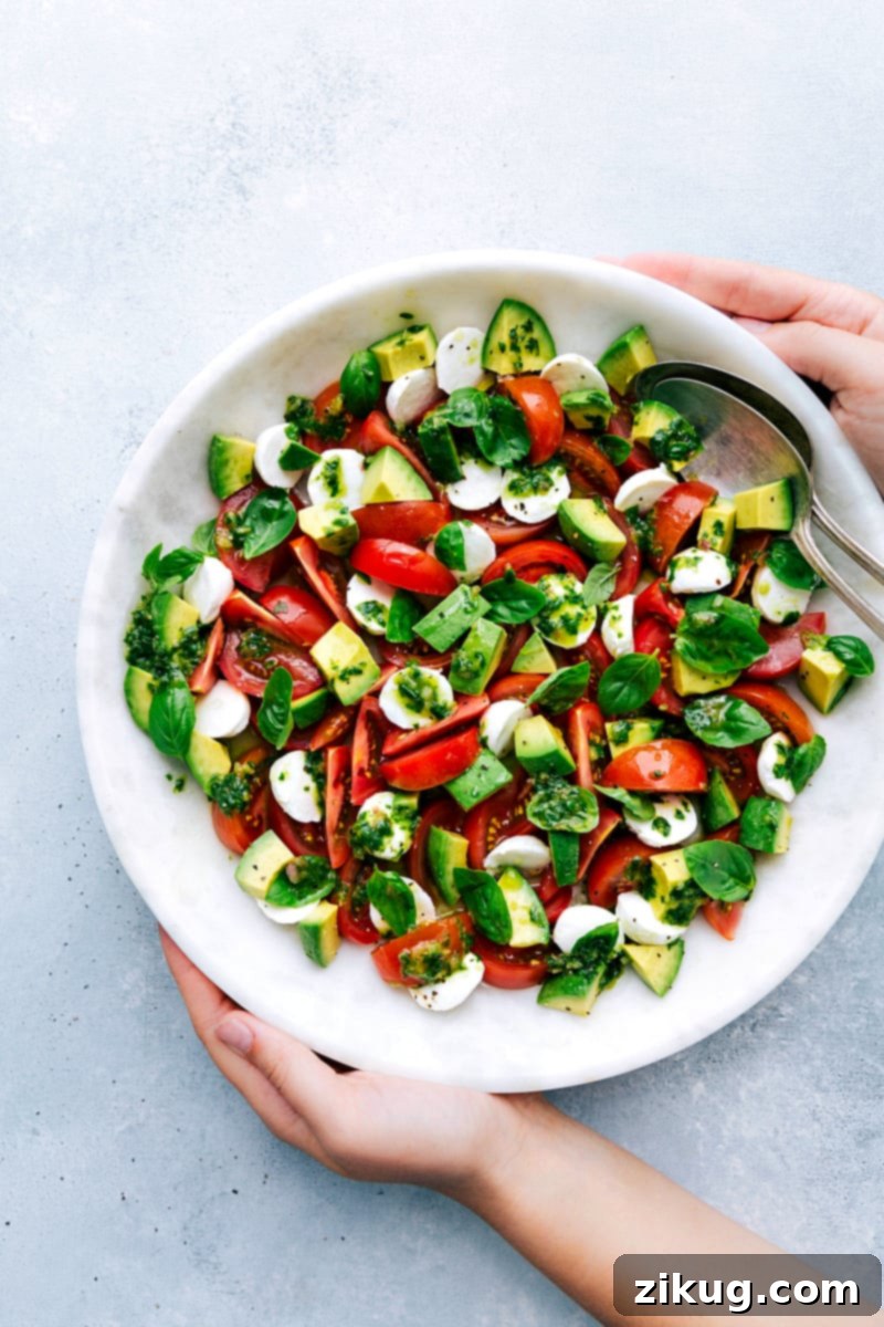 A vibrant Caprese Salad in a bowl, generously tossed with basil vinaigrette and garnished with freshly torn basil leaves, showcasing its rich colors and textures.