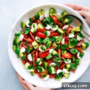 A vibrant Caprese salad featuring tomatoes, mozzarella, and avocado with a basil dressing, presented in a clean white bowl.