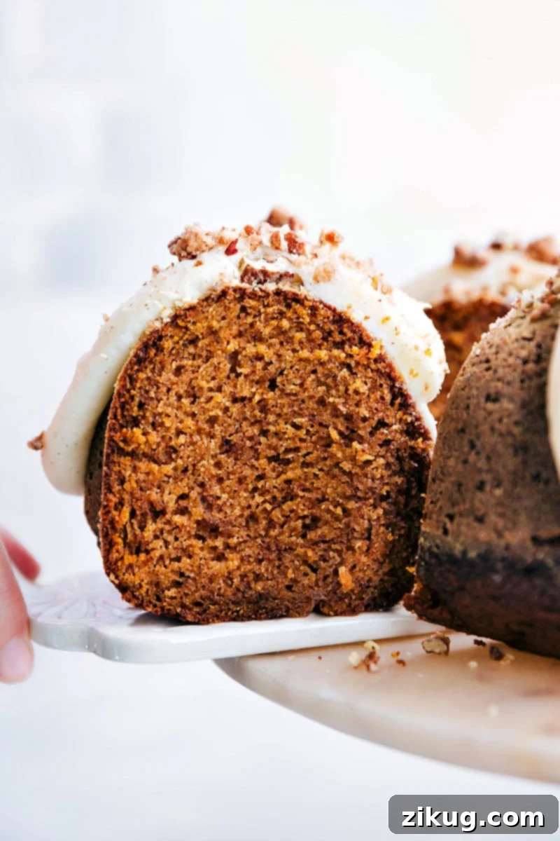 Pumpkin Cake Slice with Cream Cheese Frosting - Irresistible Moistness A glorious slice of moist pumpkin cake, generously slathered with creamy white cream cheese frosting, being lifted from a bundt cake. The soft, fluffy interior with hints of spice is perfectly visible, ready to be enjoyed.