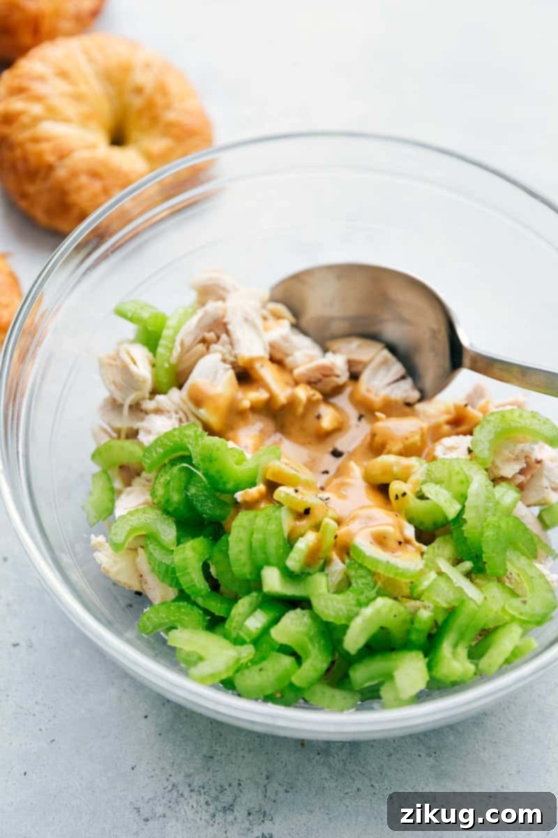 Mixing Honey Mustard Chicken Salad: Step-by-Step Guide A bowl of Honey Mustard Chicken Salad mixture being gently stirred, with fresh croissant rolls visible in the background, symbolizing the anticipation of a delicious meal. The ingredients are perfectly combined for optimal flavor.