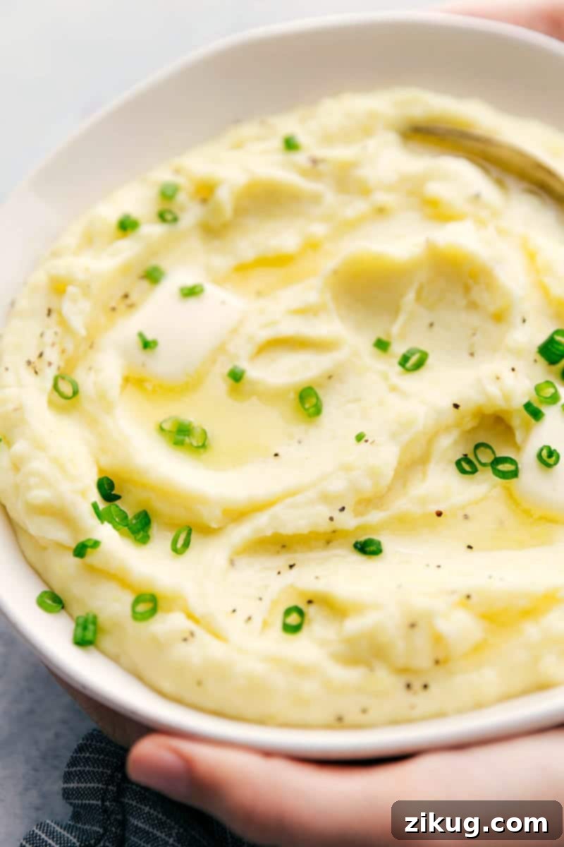 This rich and creamy Mashed Potatoes recipe also includes tips and tricks on how to make the BEST Mashed Potatoes. A large bowl of golden mashed potatoes with a serving spoon, ready for a family meal.
