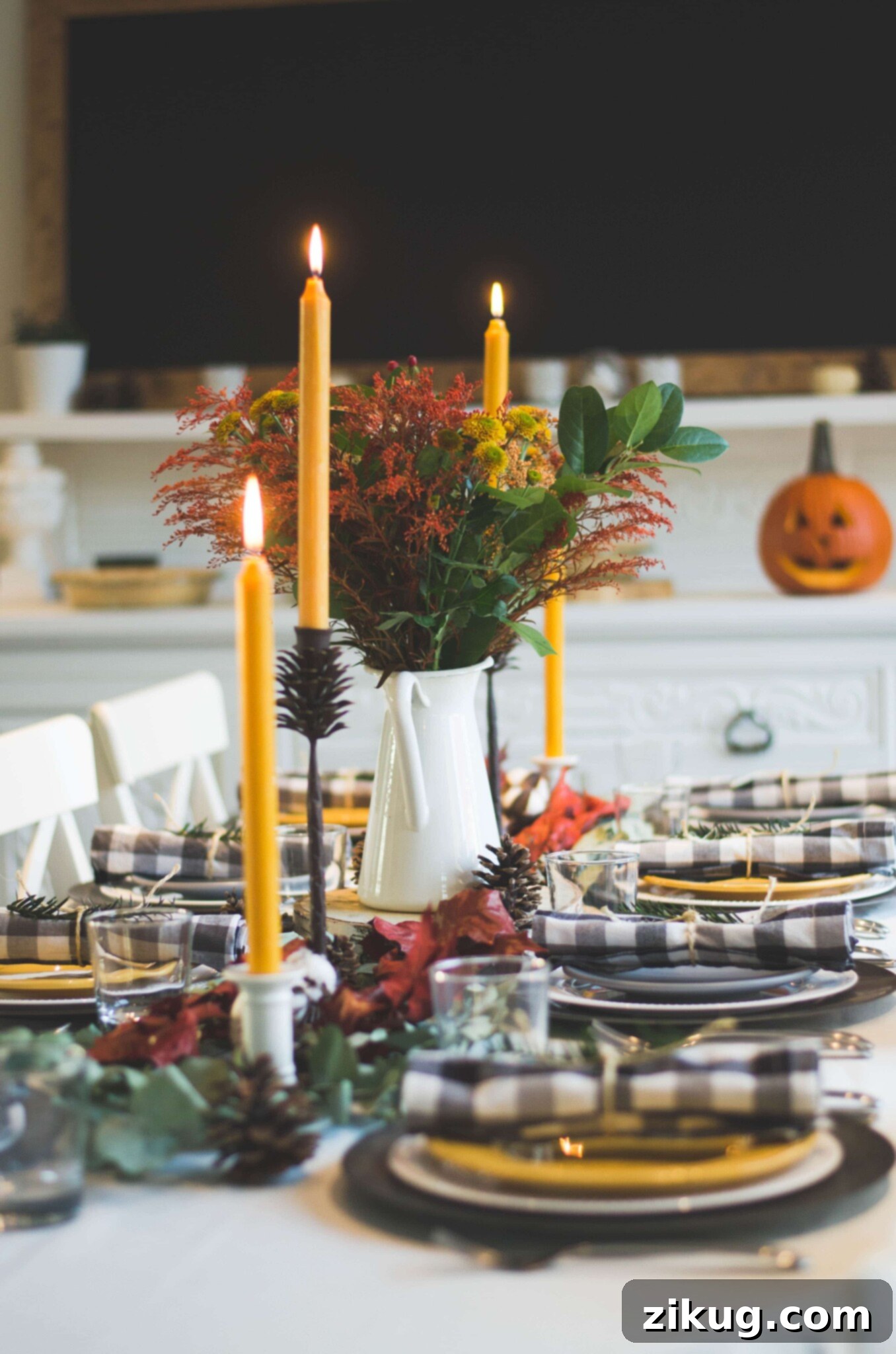 A Thanksgiving tablescape with plates, napkins, candles, and seasonal flowers, highlighting elegant setting ideas for a festive dinner. Setting the table is an important part of our Thanksgiving planning guide.
