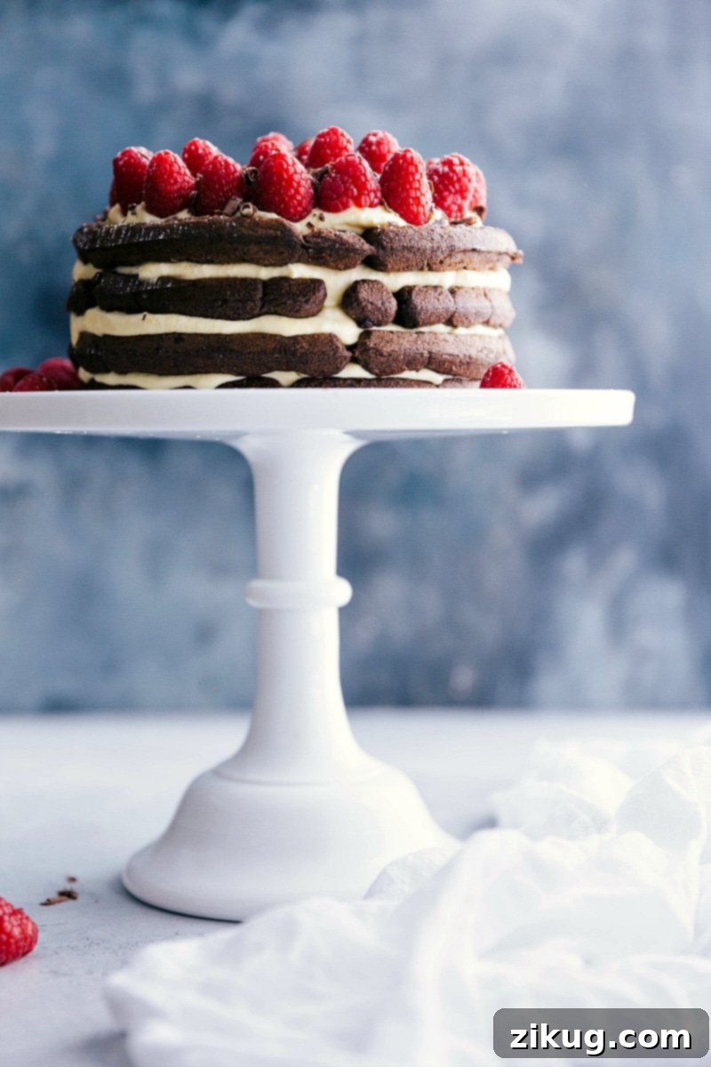 Waffle cake displayed on a cake stand, adorned with vibrant fresh raspberries and a light dusting of powdered sugar on top.