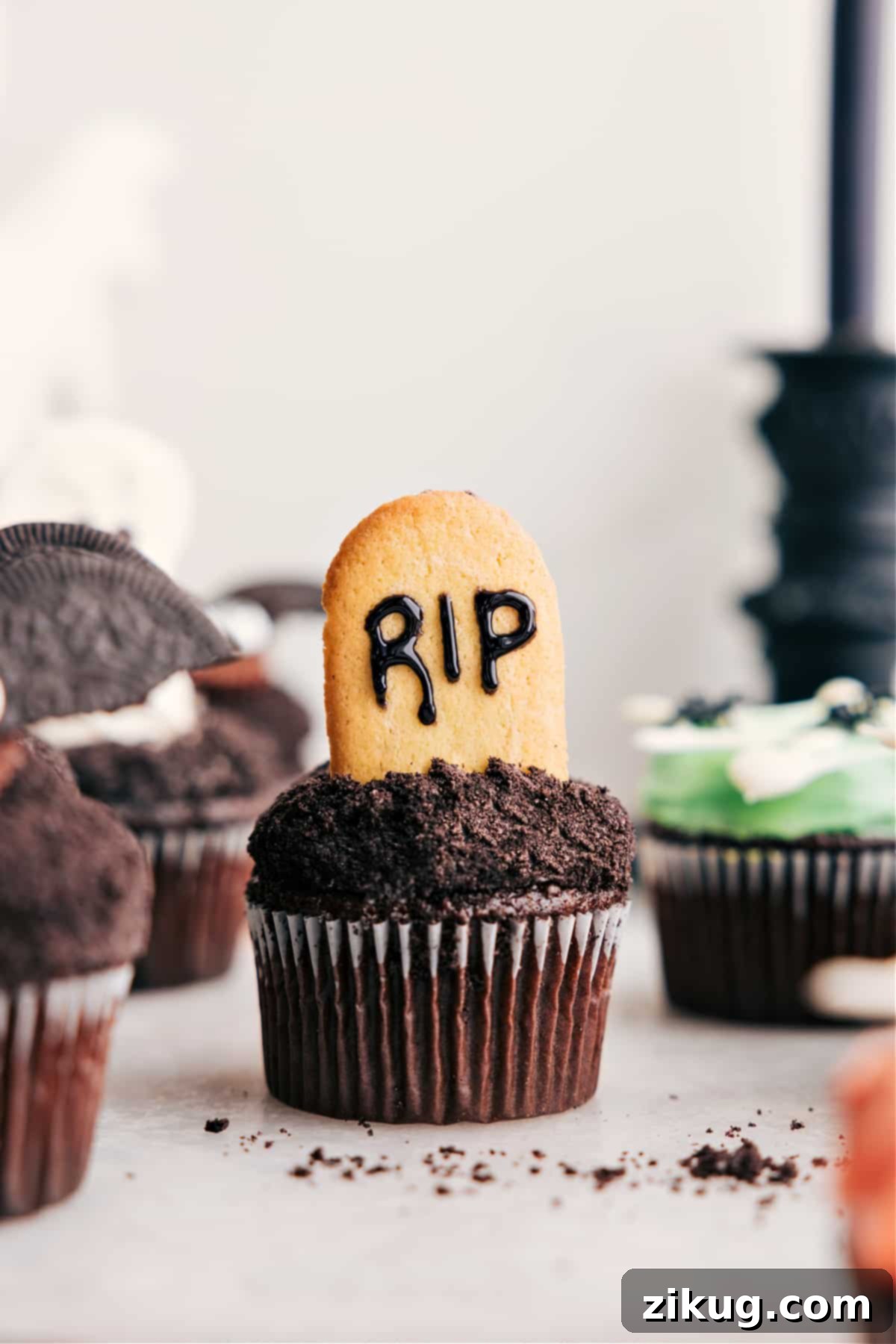 A tombstone-themed treat featuring Milano cookies inscribed with 'RIP' in black frosting, embedded in a frosted cupcake.