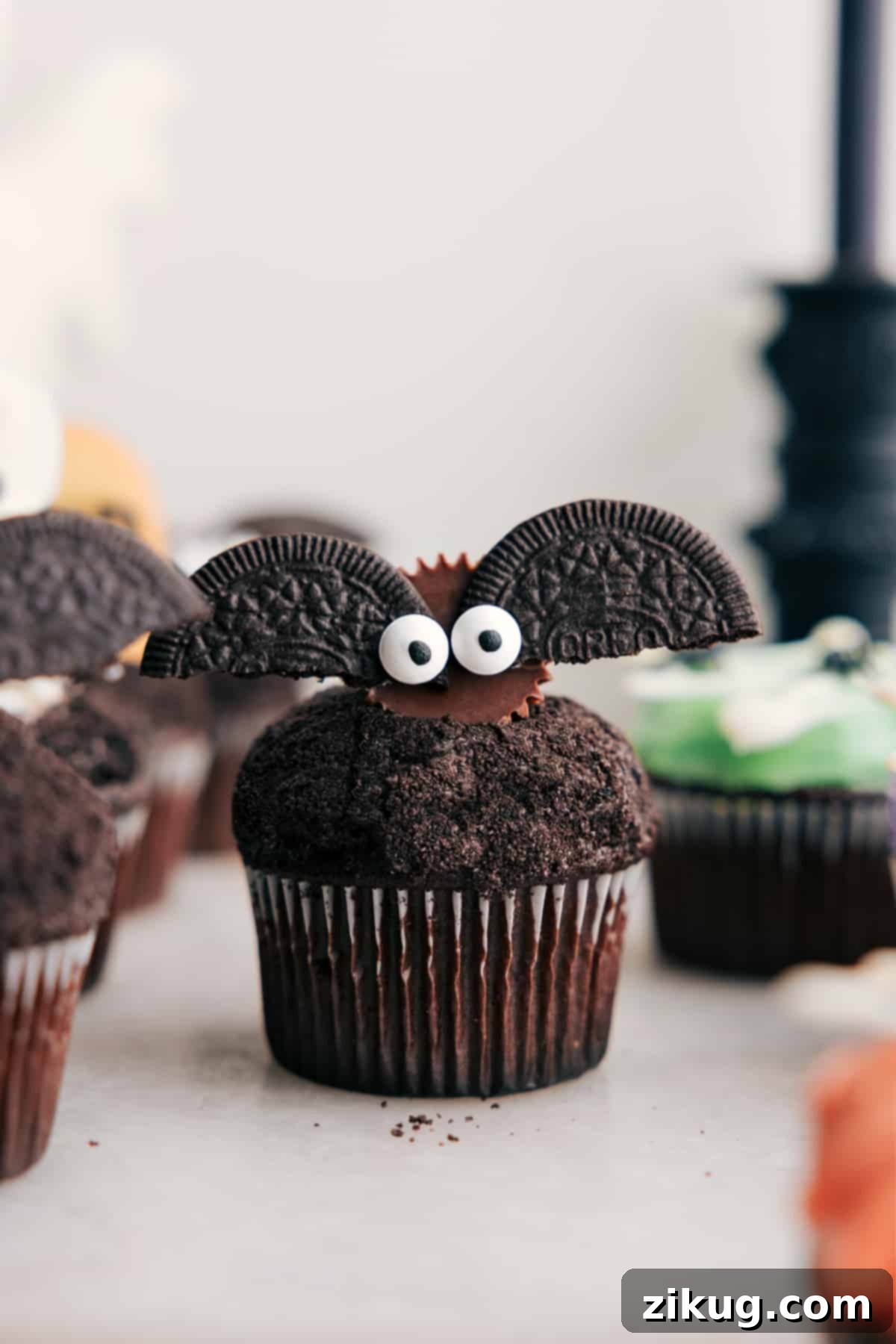 Close-up of cute bat Halloween cupcakes made with mini Reese's, Oreos, and edible eyes on a frosted cupcake.