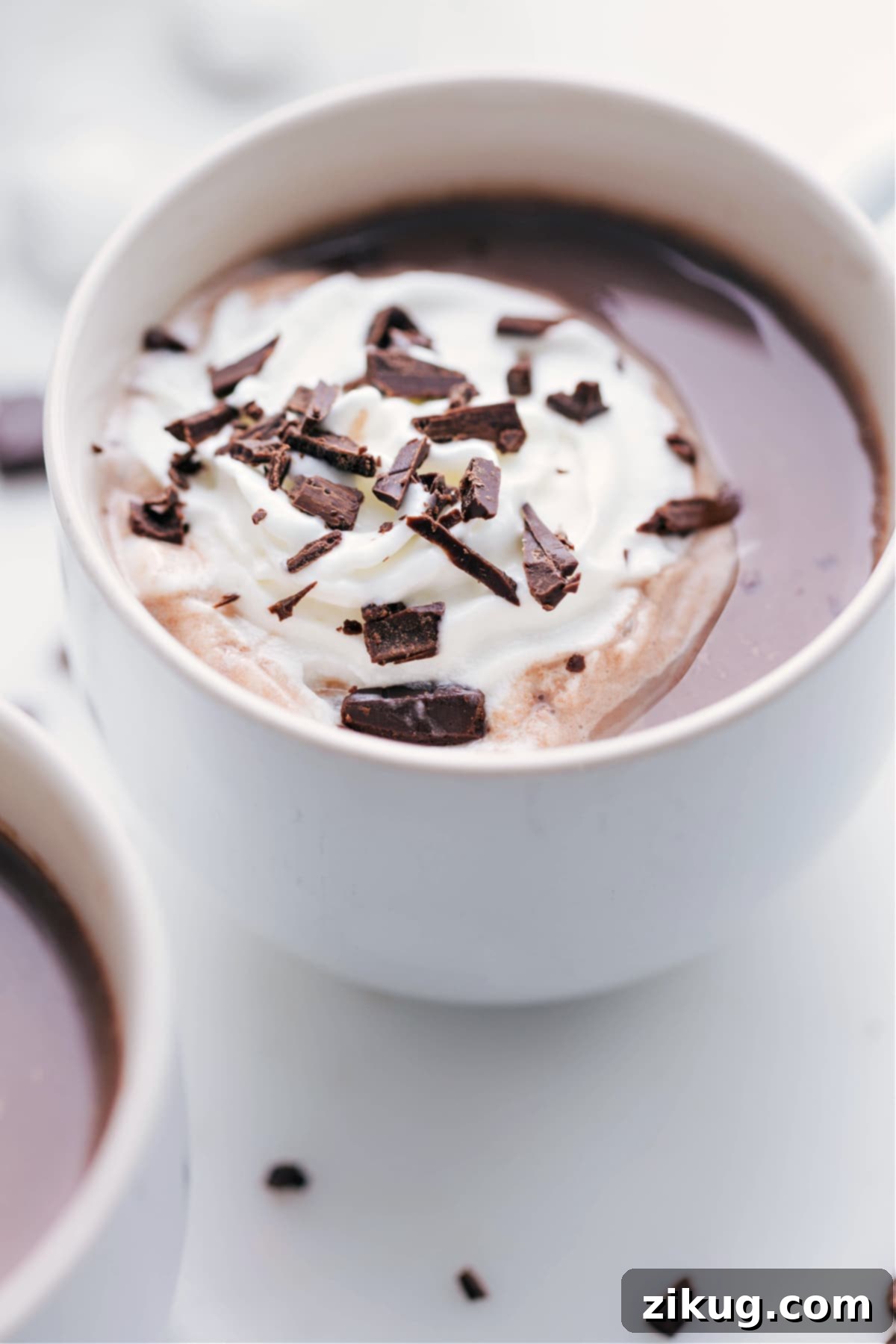 Mug filled with a delicious hot chocolate topped with a dollop of whipped cream and delicate chocolate shavings.