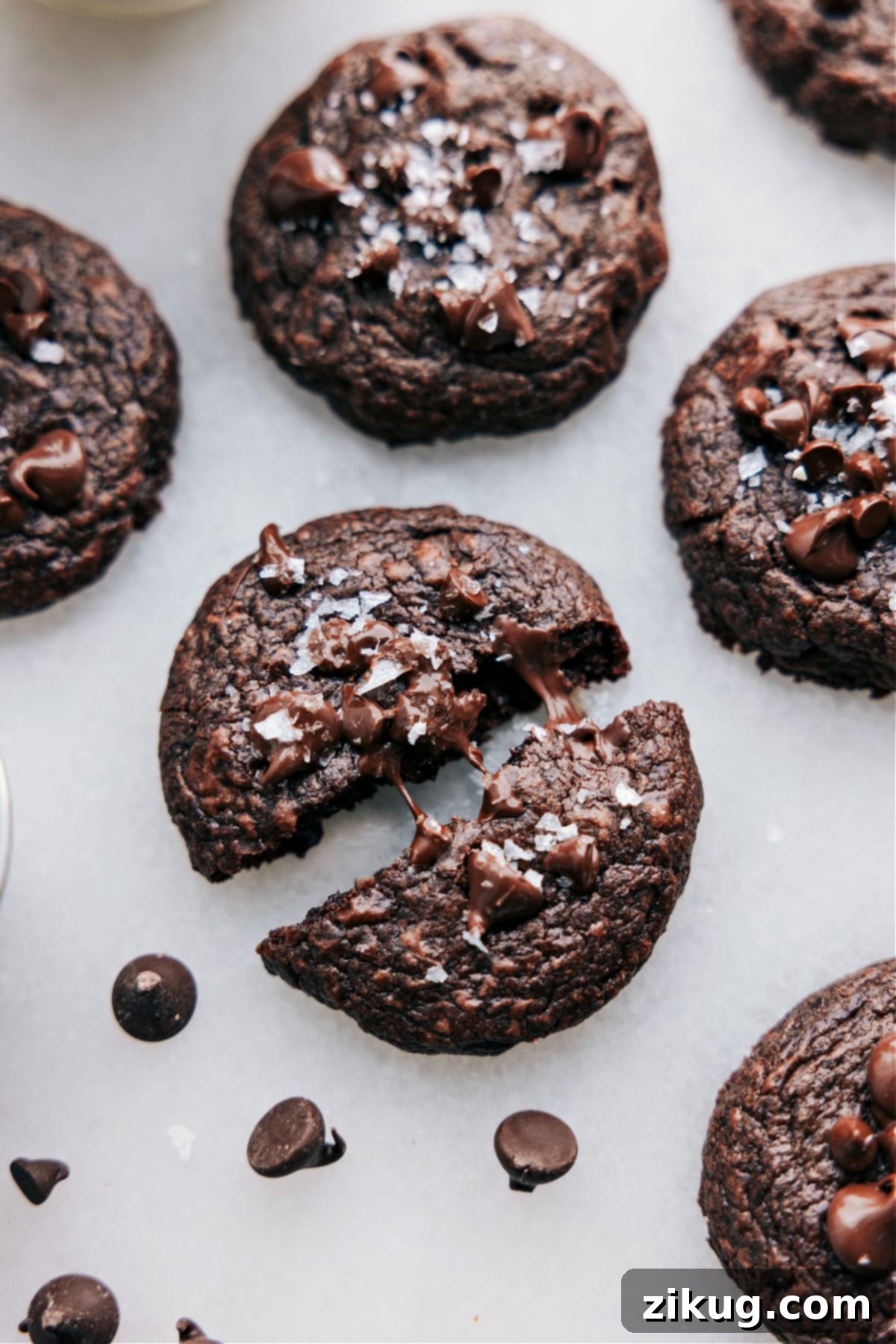 The Best Fudgy Brownie Cookie Recipe Warm brownie cookies on a rustic board, one broken open to reveal its gooey, melted chocolate center.
