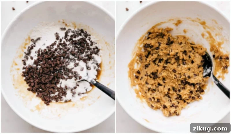 A large mixing bowl filled with creamy, light brown edible cookie dough, rich with chocolate chips. A spatula is gently folding in the final ingredients of toasted flour and mini chocolate chips, ensuring a smooth and uniform mixture, signifying the completion of the dough preparation.