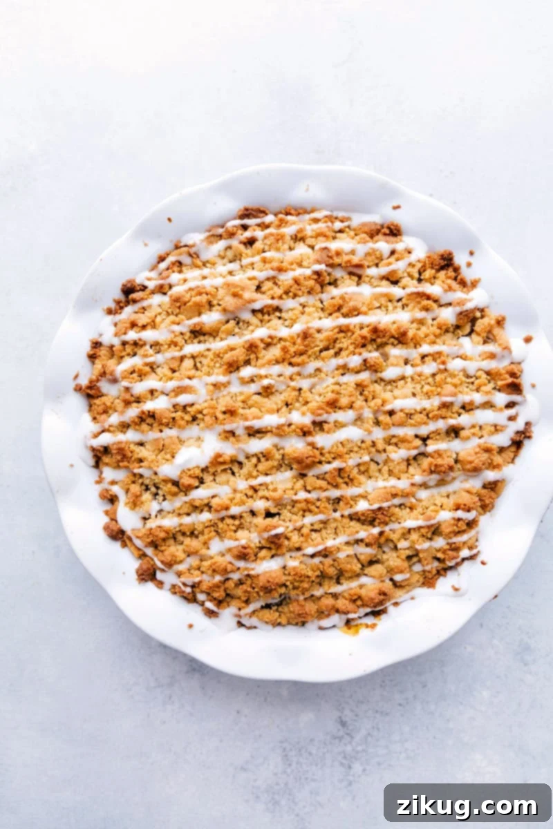 A delicious and easy-to-make Cinnamon Roll Apple Pie, featuring a unique cinnamon roll crust, apple pie filling, and a sweet glaze. Overhead image of a beautifully baked Cinnamon Roll Apple Pie, showing its golden crumble and inviting glaze