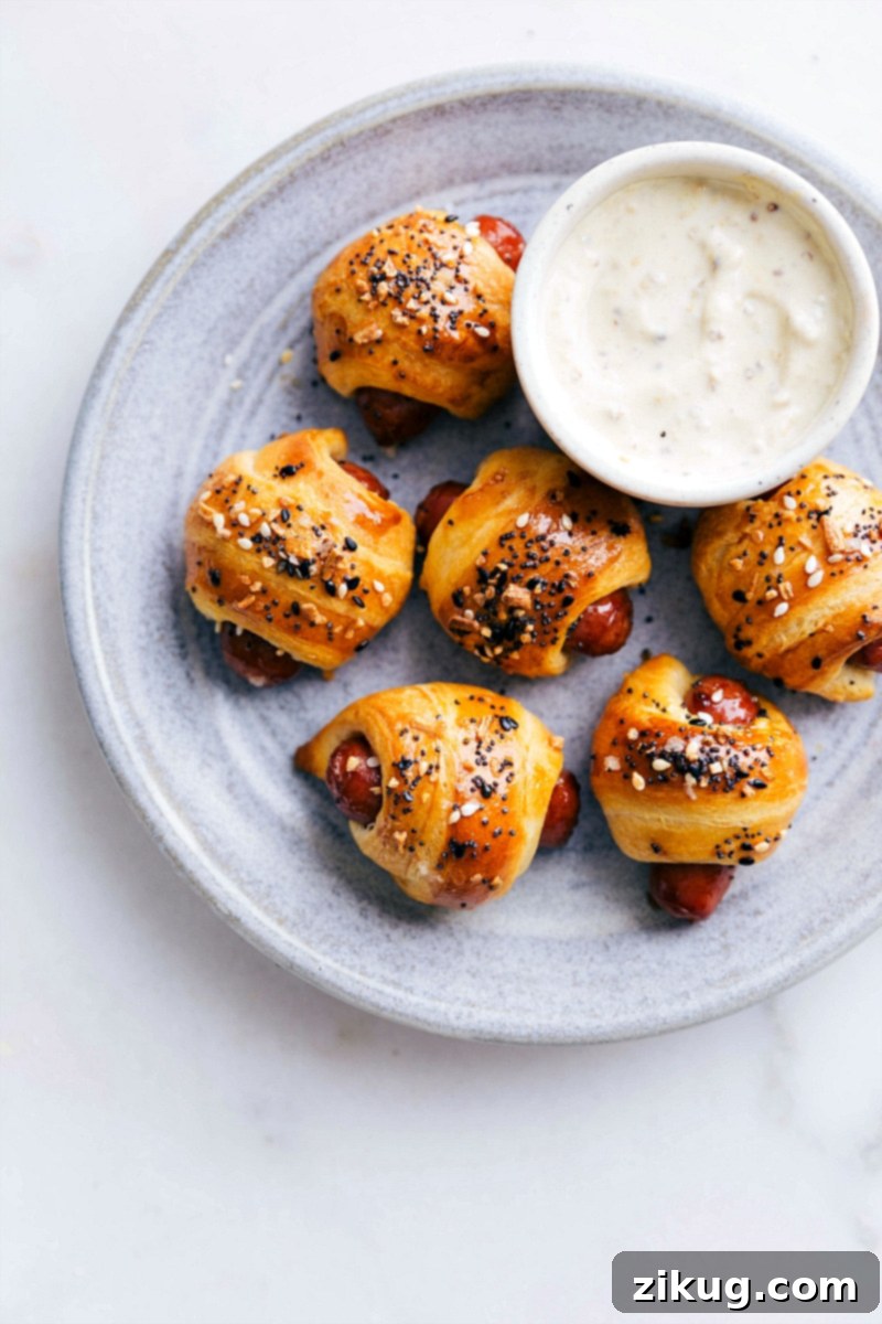 Golden-brown Pigs in a Blanket with everything bagel seasoning, served on a white platter, ready to be enjoyed as a party appetizer.