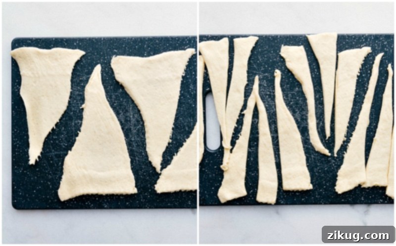 Process shot showing a tube of crescent roll dough unrolled and being cut lengthwise into smaller strips, preparing for pigs in a blanket assembly.