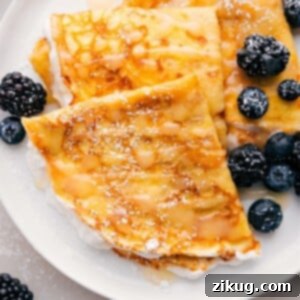 Plate of three crepes with fresh berries and maple syrup drizzled on top, ready to be served.