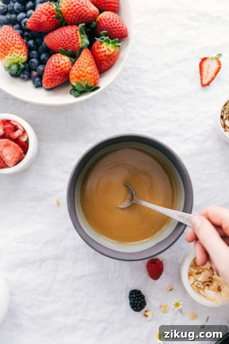 Homemade Vanilla Sauce: Quick & Easy 5-Ingredient Recipe for Bread Pudding, Waffles, and Pancakes Overhead photo of a creamy vanilla sauce in a small white bowl, garnished with fresh berries like raspberries and blueberries, making it an inviting dessert or breakfast topping.