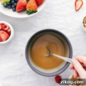 A small white bowl filled with creamy vanilla sauce, surrounded by fresh raspberries and blueberries, ready to be served over breakfast or dessert.