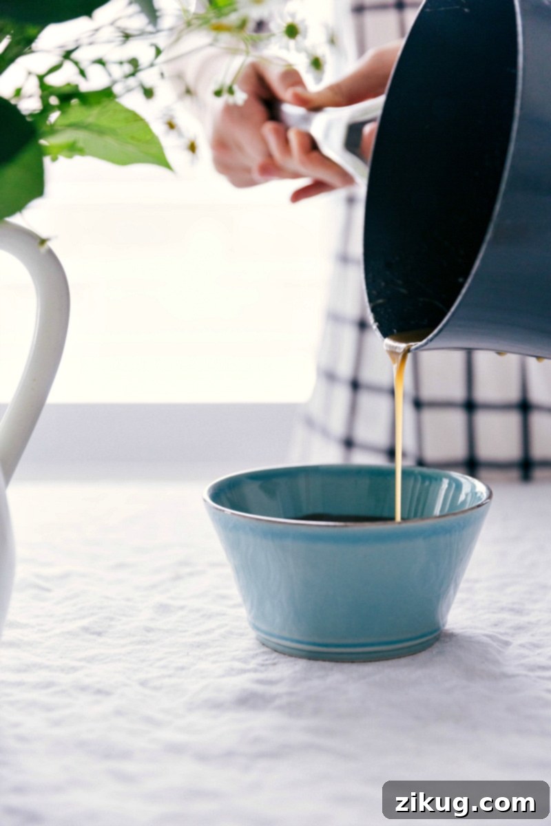 Serving Homemade Vanilla Sauce: Freshly Poured and Ready Image of the freshly made, warm vanilla sauce being poured from a saucepan into a small ceramic bowl, ready to be served over breakfast or dessert.