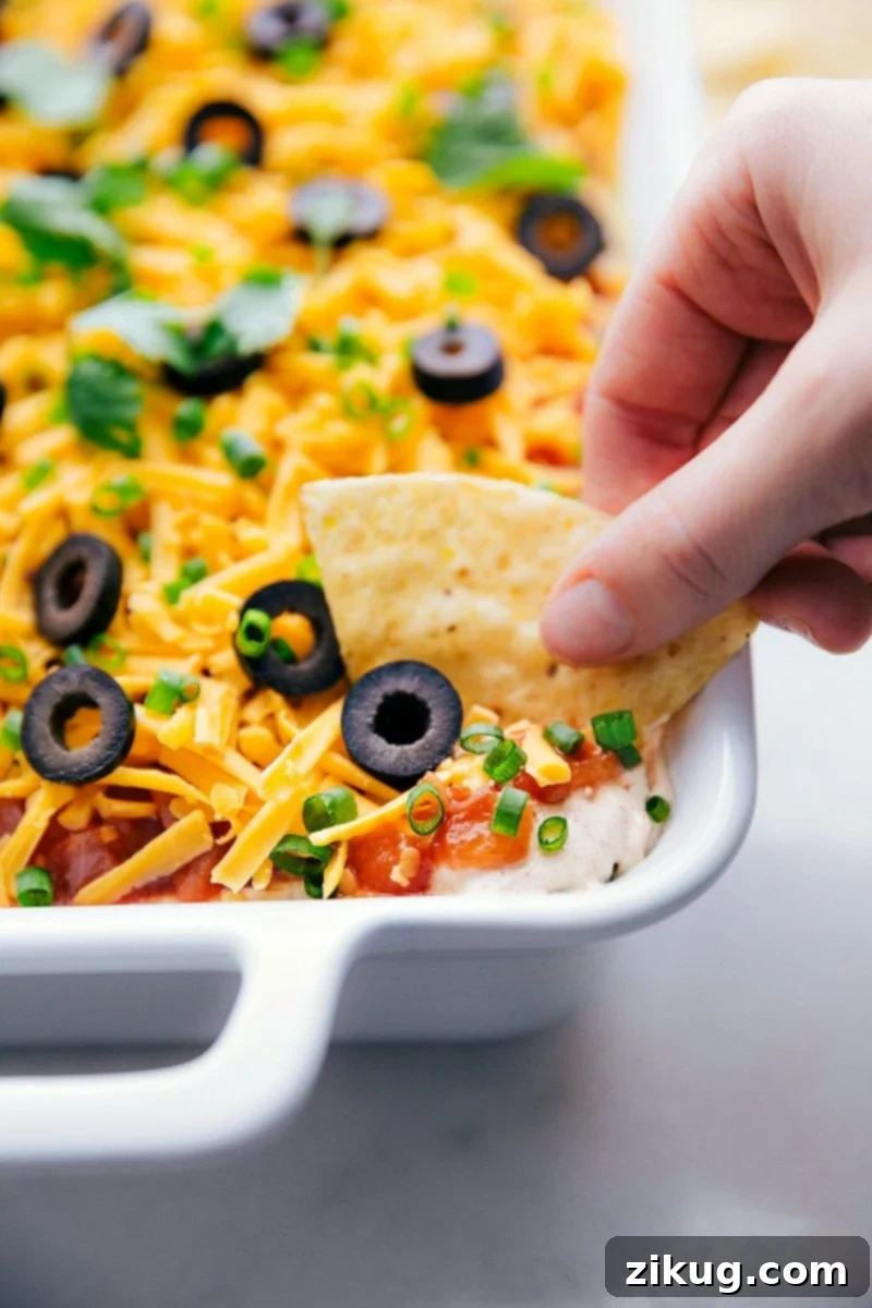 The ultimate game-day and party 7-Layer Bean Dip recipe A scoop of vibrant 7-Layer Bean Dip on a tortilla chip, showcasing all the delicious layers.